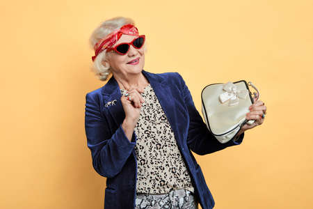 blonde cool grandmother looking at her new white bag. isolated yellow nbackground. studio shot.