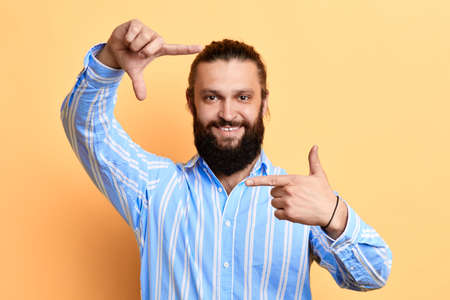 happy positive handsome young man making frame with fingers isolated on a yellow background. camera. man is pretending that he is taking a photoの写真素材