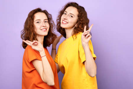 gorgeous brunette women looking at camera with smile and showing peace sign with fingers isolated over blue backgroundの写真素材