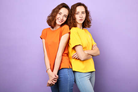 Two cheerful positive girls twins smiling over blue background.sad unhappy sister with crossed arms...