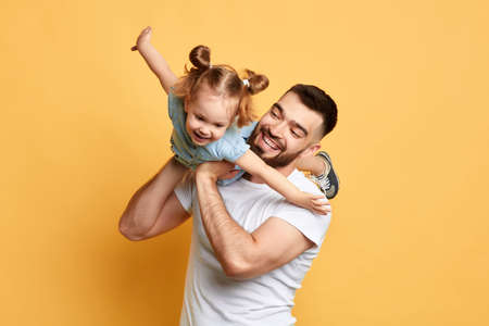 cheerful happy man teaching sweet lovely daughter to fly like a plane. close up photo. isolated yellow background. studio shot, happy moments with best fatherの写真素材