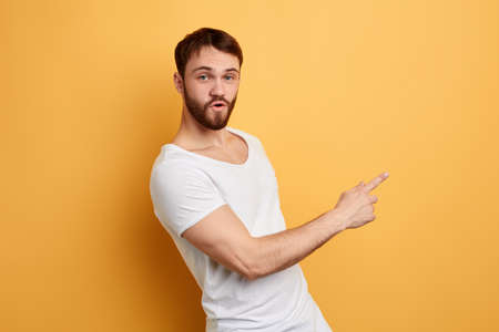 pleasant attractive young man in white T-shit pointing at copy space, place for advertisement.text hereの写真素材