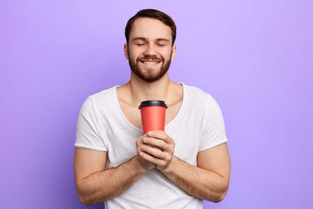 pleasant man drinking his favourite coffee. close up portrait. isolated blue background, studio...
