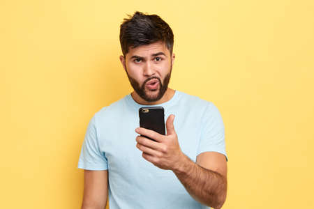 puzzled guy using his mobile phone. close up portrait. young bearded man has problems with gadget,...