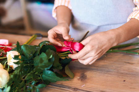 close up cropped photo of female florist making bunch and tying ribbon at flower shop.の写真素材