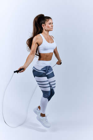 brunette active sportswoman jumping with skipping rope in the sport center. full length side view...