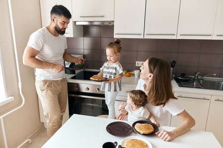 little hardworking girl treating her parents and little sister with yummy pancakes. close up photo.の写真素材
