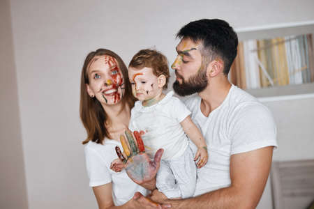 young couple with painted faces holding their little child in hands after art class. close up photo
