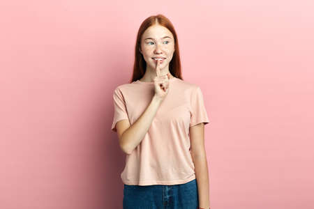 Portrait of beautiful young woman holding index finger on lips, asking to keep silence or not tell...