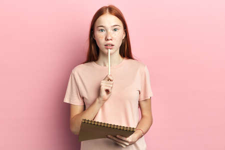 serious attractive shocked girl with freckles looking at the camera.woman with a pen on her lips hesitating to answer the question during examの写真素材