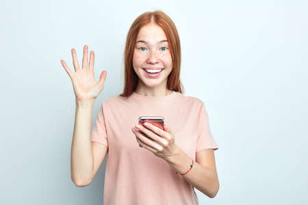happy ginger girl waving her hand while using her smart phone, hi, hello, good buy, girl greeting...