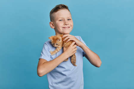 positive kid embracing his orange kitten and looking at the camera, close up portrait, animal lover