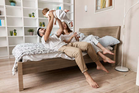 daddy and mommy raising l little child while lying on bed at home, side view photo, spare time, . lifestyle, free timeの写真素材