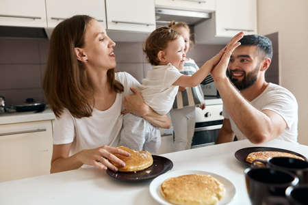 little girl giving high five to her adoirable bearded dad while having breakfast in the kitchne, positive feeling and emotion. close up photoの写真素材