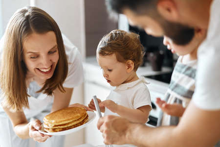 cheerful beautiful woman giving pancakes to her nice kid. close up side view photo. help yourself.の写真素材