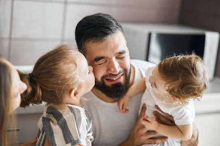 two adorable daughters kissing their daddy in the kitchen. close up photo. warm, tender feeling and...