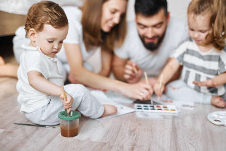 little girl holding paitbrush and dipping it in the water, close up cropped photo. blurred backgroundの写真素材