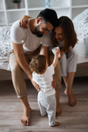 attractive cheerful parents teaching baby to walk, full length photo.first steps.happiness conceptの写真素材