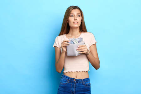 beautiful young woman holding coin purse and looking aside, girl has stolen money from bank,...