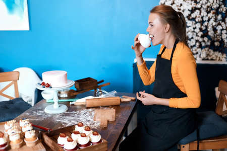 funny blonde cook degustating cupcakes, eating dessert, close up side view photoの写真素材