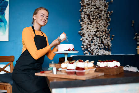 smiling blonde girl enjoying decorating dessert for a party. close up photo. favourite job, hobby,...