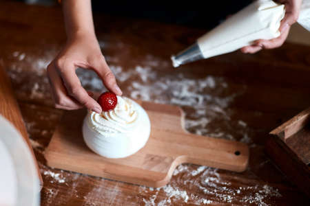 girl putting berry on the top of muffin with cream, close up cropped photoの写真素材