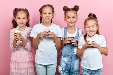 adorable positive little girls holding dessert posing to the camera, happy childhood, party concept, isolated pink backgroundの写真素材