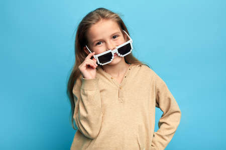 cheerful nice pretty girl with hands on her hips taking off sunglasses. close up portrait, isolated blue background, studio shotの写真素材