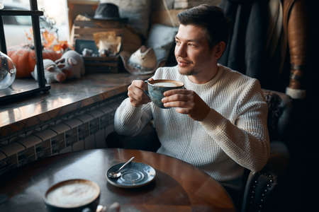 awesome man sitting in caffe and drinking hot tea in front of window, close up side view photo, good...