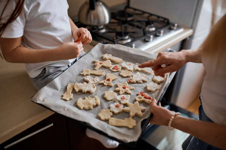 little adorable girl and her mother decorating cookies before putting baking sheet into the oven, close up side view cropped photo.designの写真素材