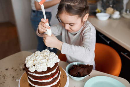 child squeezing cream from pastry bag on the top of cake. close up photo