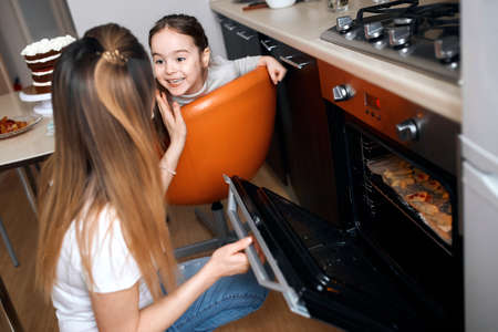 The little girl waiting for the preparation of tasty cookies, cheerful girl sitting on the chair and...