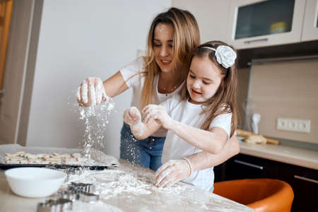 little girl and her mother get pleasure from playing with flour, close up photo.flour falling down on the table.の写真素材