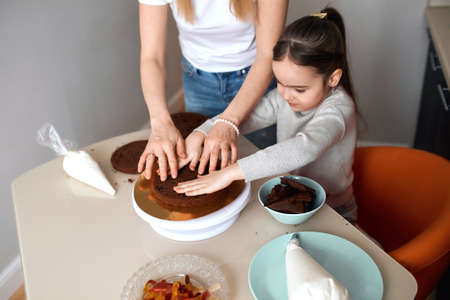 little girl and her mother putting pieces of cake on each other, close up side view photo, process of cooking yummy cake, weekend, preparation for holiday, kid pressing sponge with palmsの写真素材