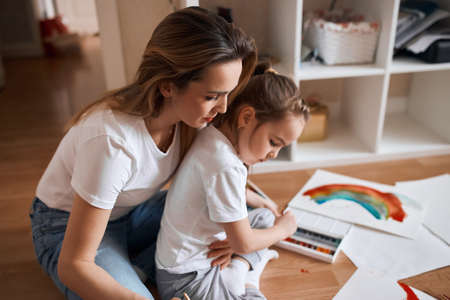 young woman giving advice recommendations while her little kid is painting, close up side view photo, woman controlling drawing processの写真素材