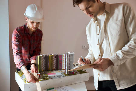 young handsome man in stylish shirt using ruler to measure the model his fair-haired colleague in white shirt writing something on notebook, notepad, close up photoの写真素材