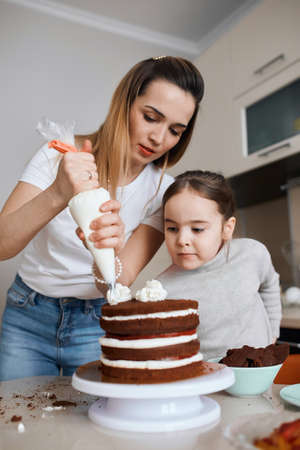 young awesome woman and little girl learning to decorate cake, people earning money by cooking dessert, close up photoの写真素材