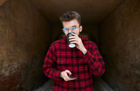 young man drinking coffee, holding his smart phone, having a rest. close up photo. gadget, technology, man tasting , sipping beverageの写真素材