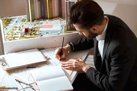 young hardworking achitecter making new building layout, close up side view photo.young man enjoying...