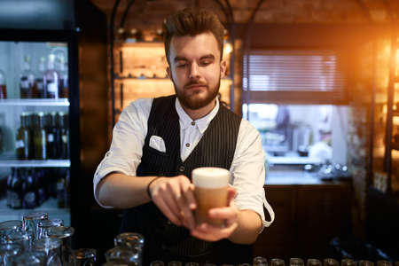 young talented bearded attractive barista has made tasty latte, close up photo. service concept, job, profession, occupation. man serves customers in a coffee shopの写真素材