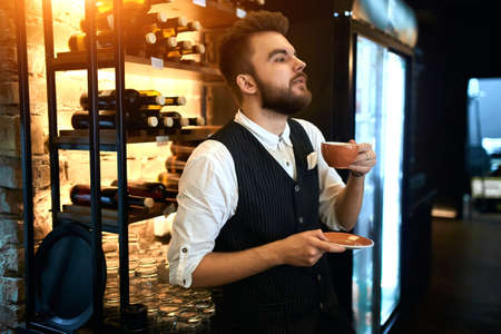young stylish man in elegant suit, shirt and vest enjoying wonderful taste of coffee, enjoyment concept. close up side view photoの写真素材