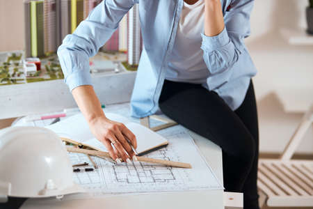 young slim stylish designer sitting on the table and measuring model with a ruler, exactly measurements. close up cropped photo.building a house conceptの写真素材