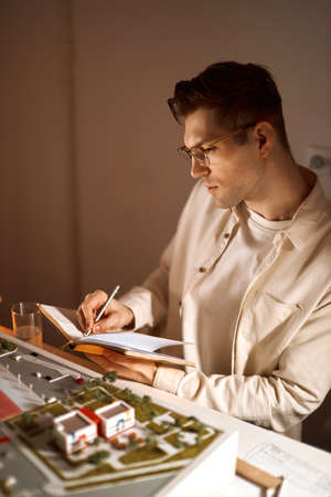 cheerful handsome architect is writing his ideas on the notebook, designer enjoying his work. close...