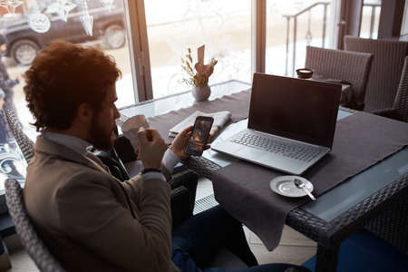 young man holding smart phone, enjoying drinking coffee while having a rest at the cafe. close up...