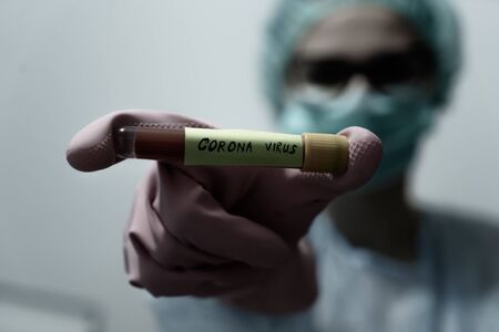 Doctor holding Blood sample of inflected coronavirus covid-19. Doctor wearing respirator mask holding a positive blood test result for the new rapidly spreading Coronavirus,の写真素材