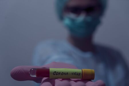 Doctor holding Blood sample of inflected coronavirus covid-19. Doctor wearing respirator mask holding a positive blood test result for the new rapidly spreading Coronavirus,の写真素材
