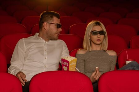 Happy couple sitting in movie theater, watching 3D movie, eating popcorn, smiling.の写真素材