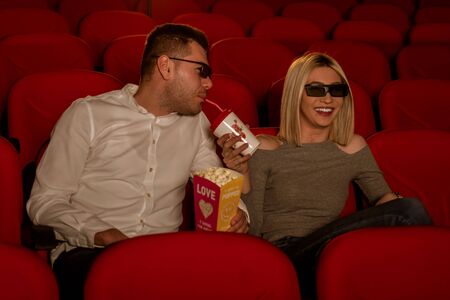 Happy couple sitting in movie theater, watching 3D movie, eating popcorn, smiling.の写真素材