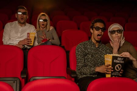 Image of laughing friends sitting in cinema watch film eating popcorn and drinking aerated sweet...