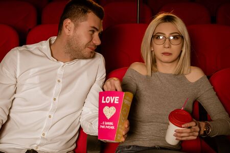 Young loving couple at the cinema watching a movie, eating popcorn, smiling.の写真素材